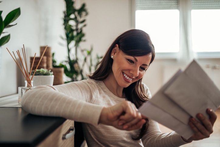 Smiling woman looking at personalized direct mail mail at home, close-up.